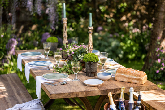 Outdoor dining table set with bread, wine, and cutlery in a garden setting