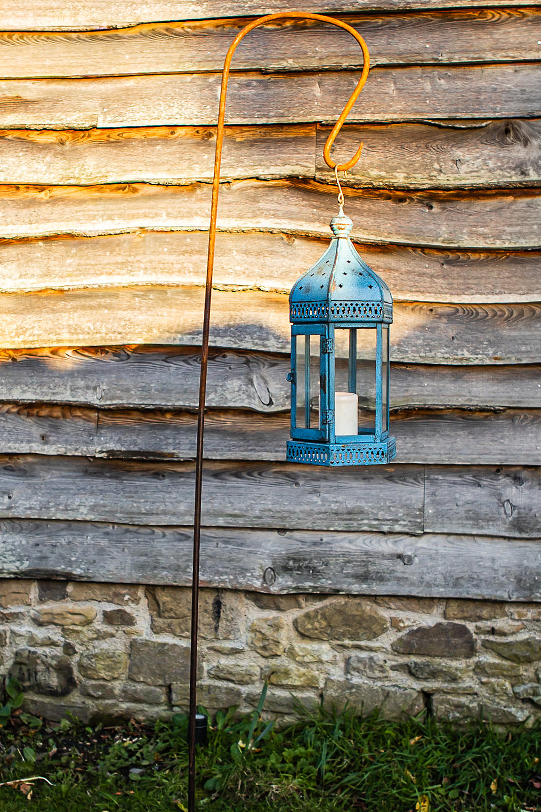 Blue lantern hanging on a wooden wall with a stone base