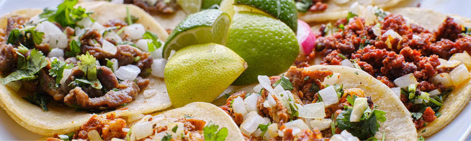 Tacos with meat, vegetables, and lime wedges on a plate