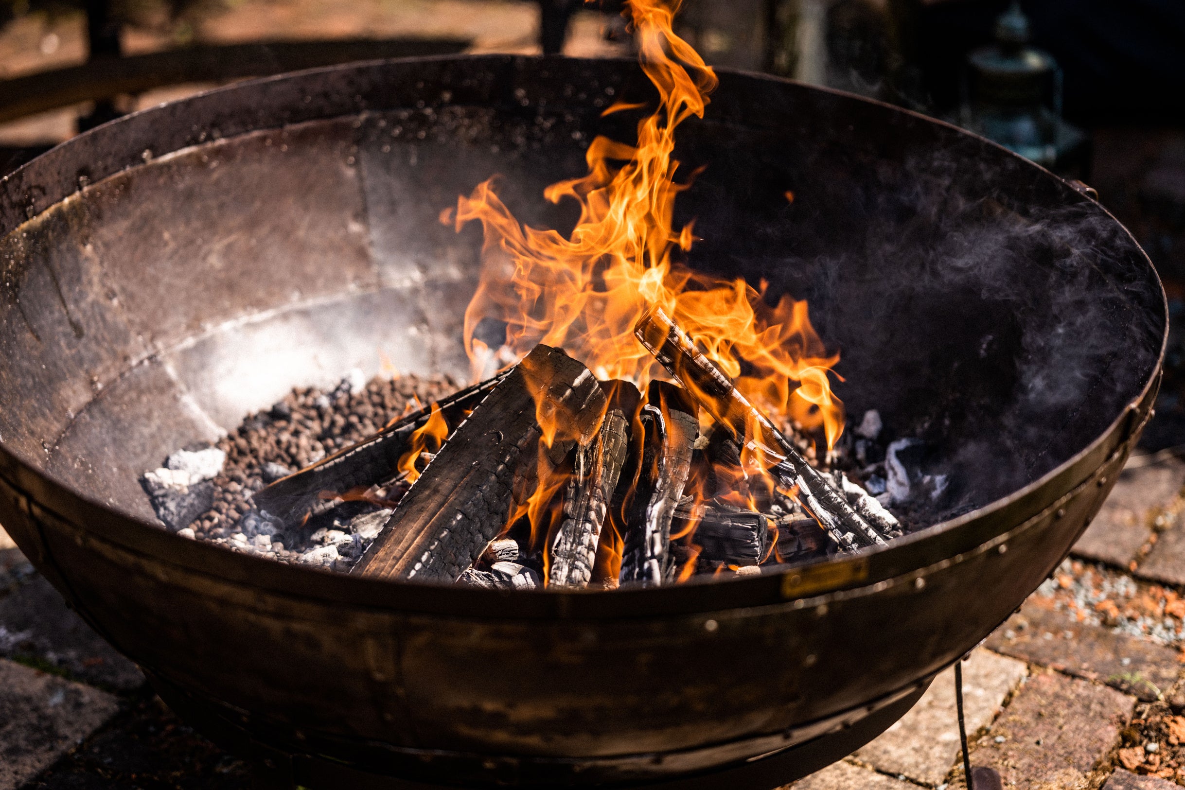 Kadai Fire pit with flames and glowing embers on a brick patio