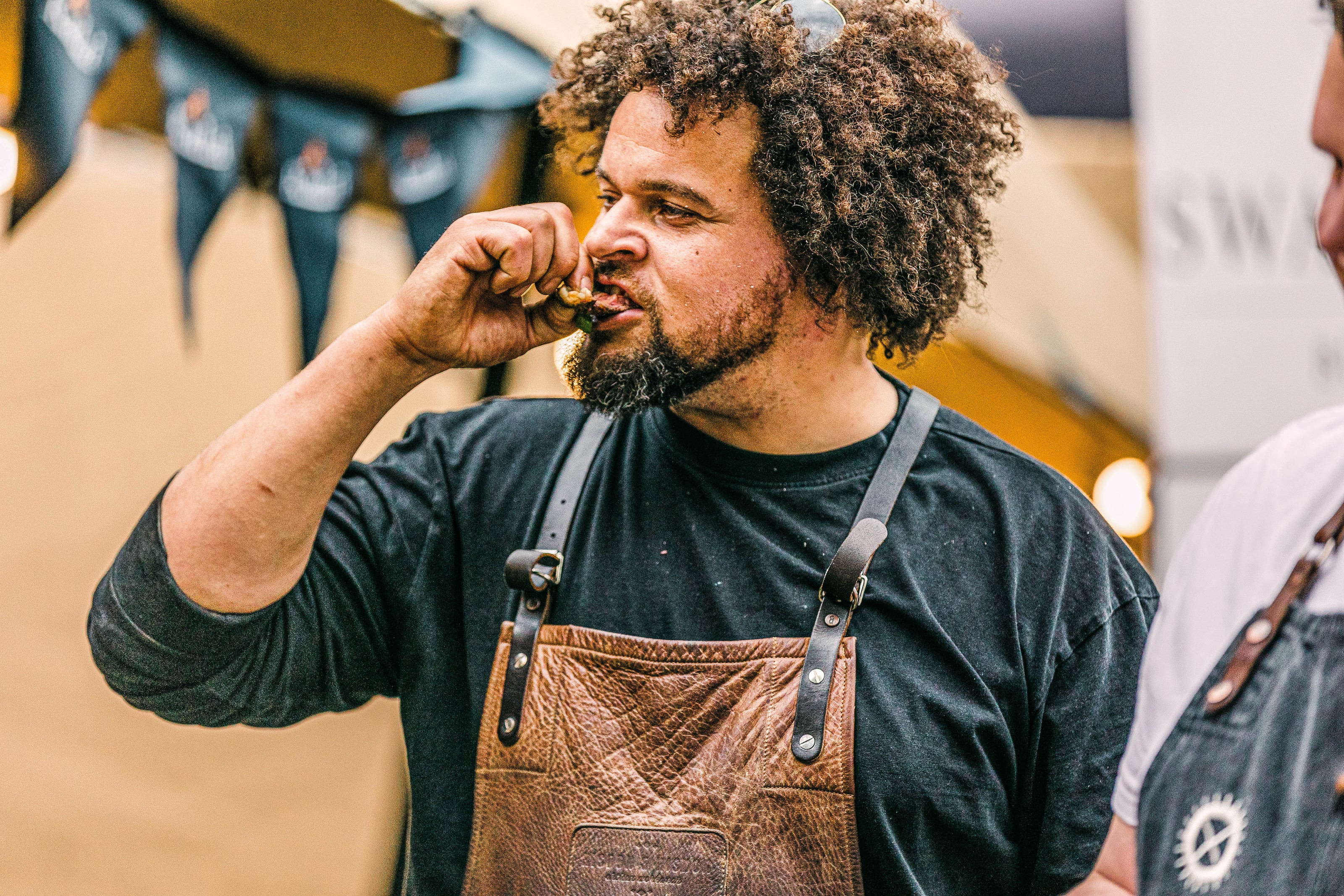 Man wearing a leather apron tasting something with a blurred background