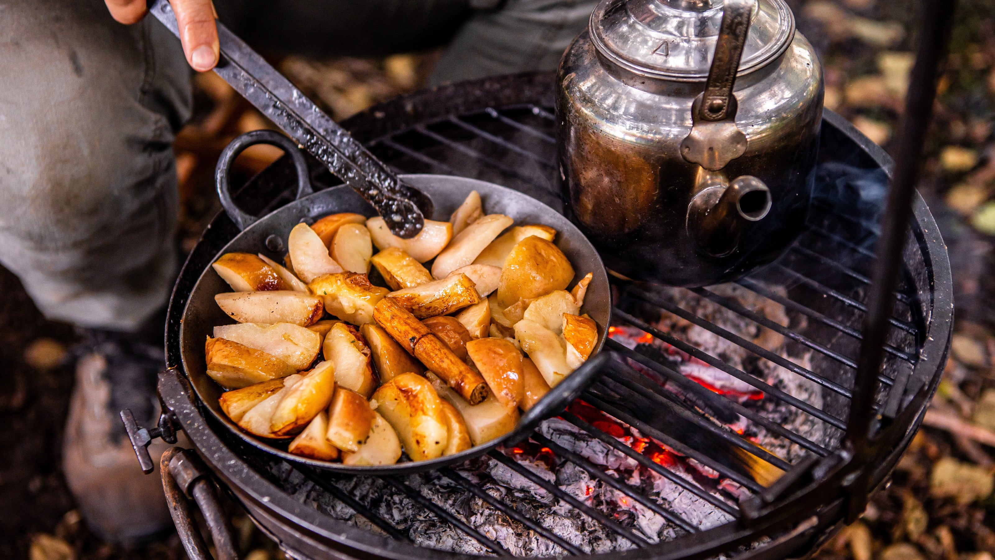 Cooking food on a portable Kadai BBQ with a kettle in an outdoor setting