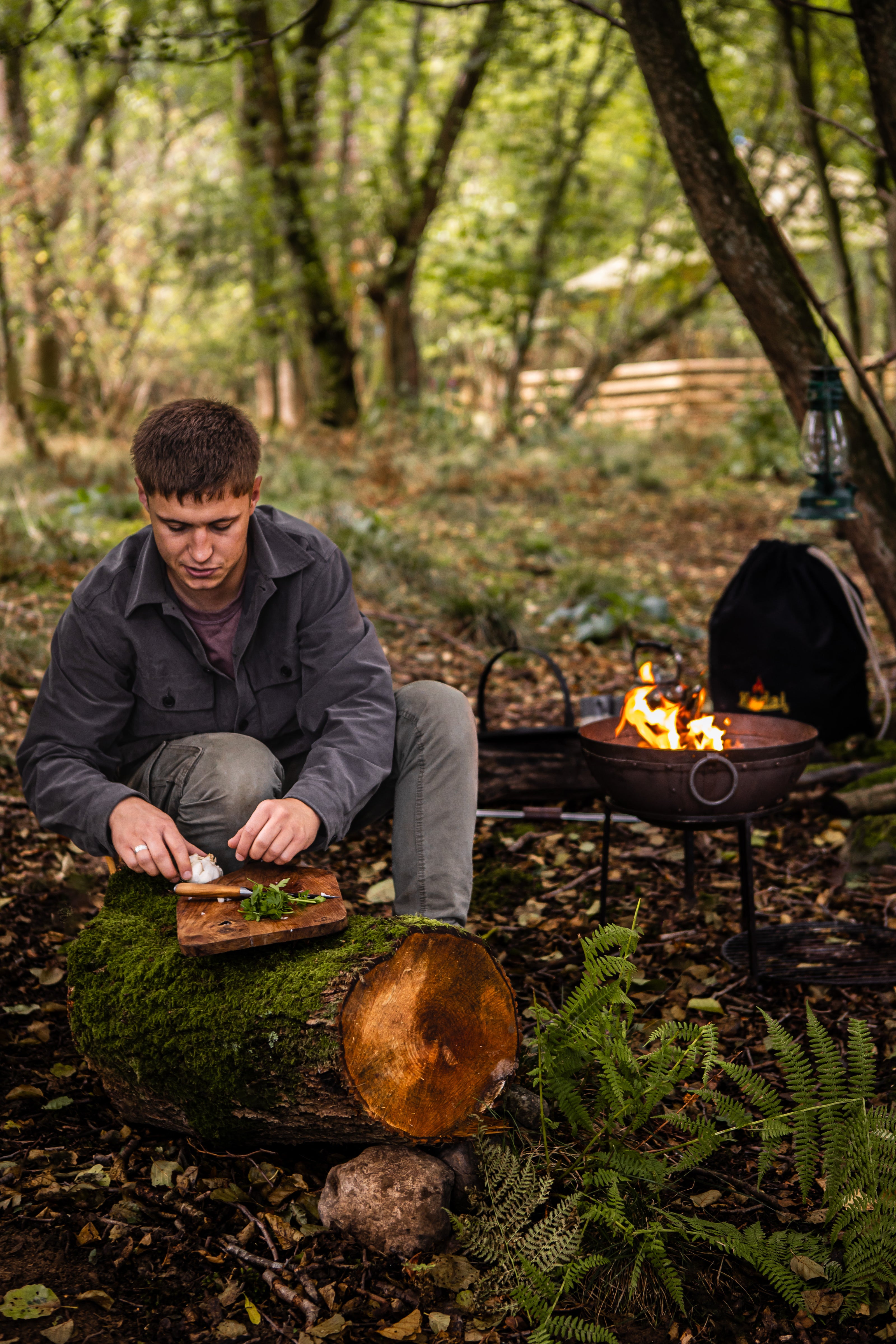 Man preparing food outdoors by a kadai travel firepit set in a forest setting