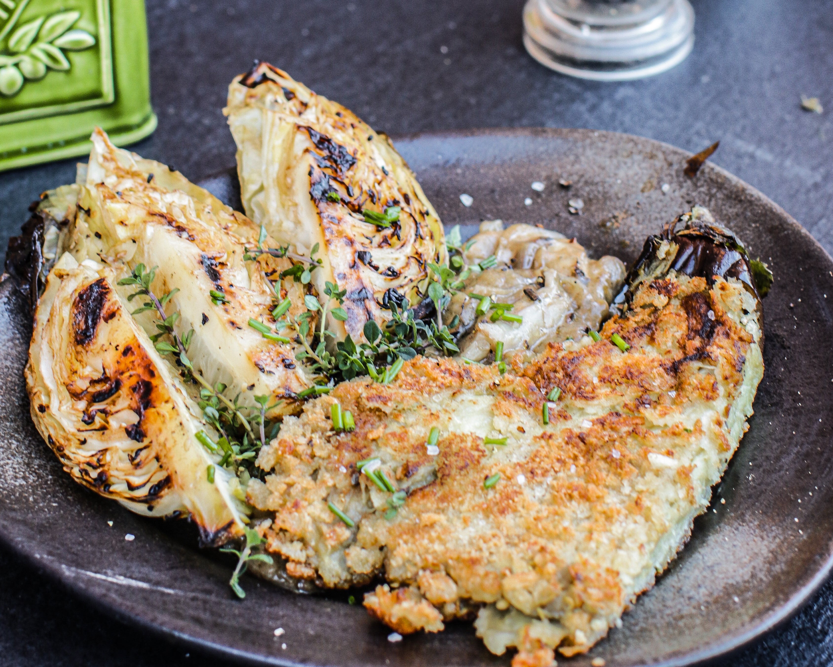 Plated dish of fried aubergine and hispi cabbage on a dark surface with a brick wall background