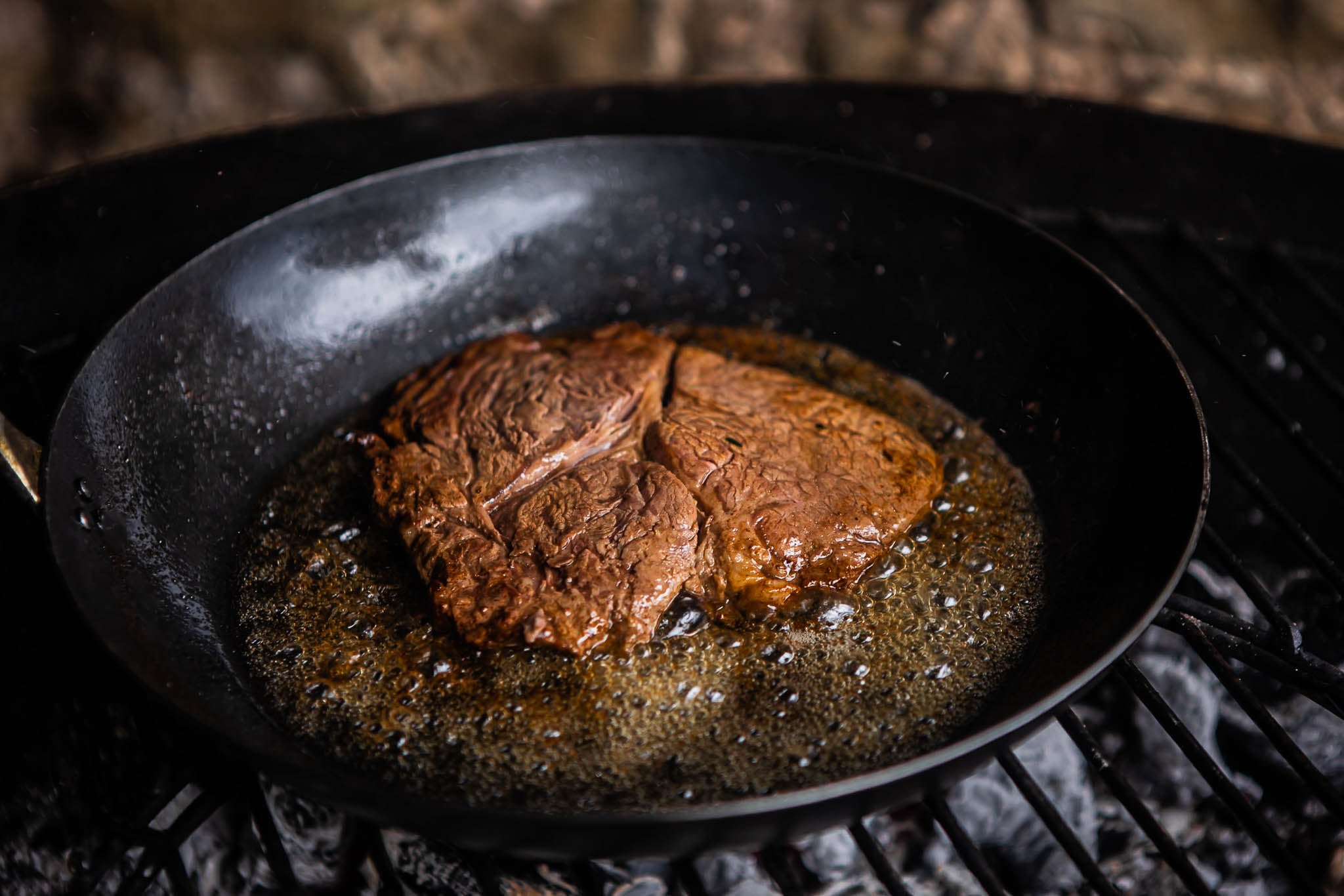 Steak being cooked in a kadai frying pan on a grill