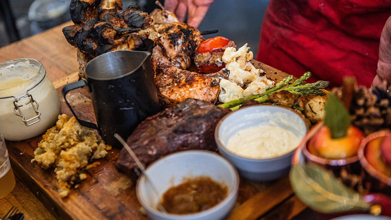 Assorted grilled meats and vegetables on a wooden board with side dishes.