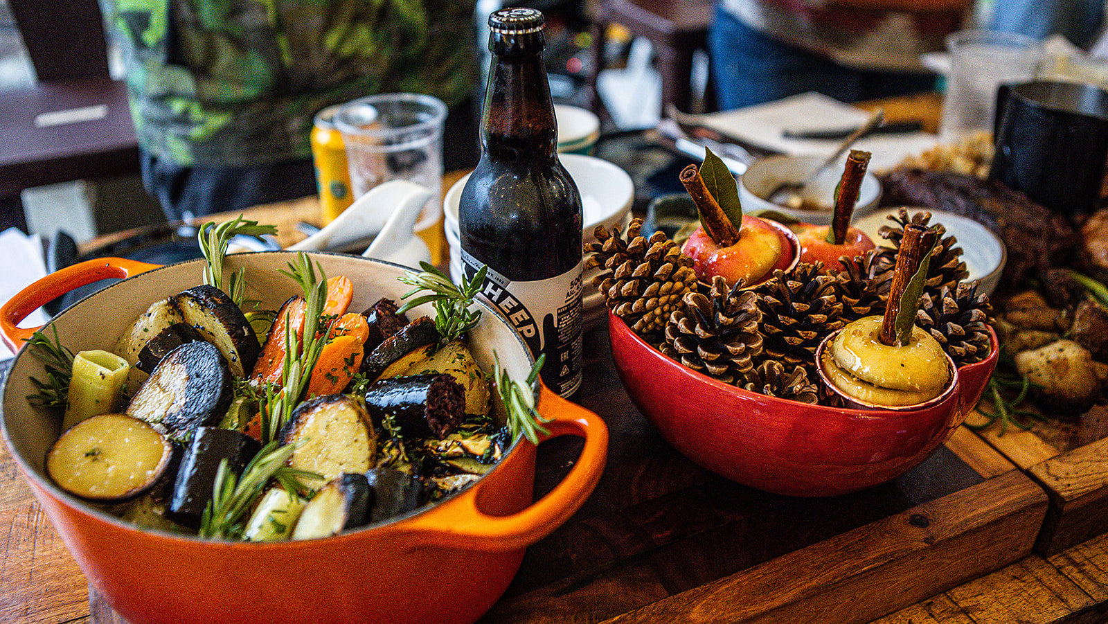 Dishes of roasted vegetables and a bottle of beer on a wooden table.