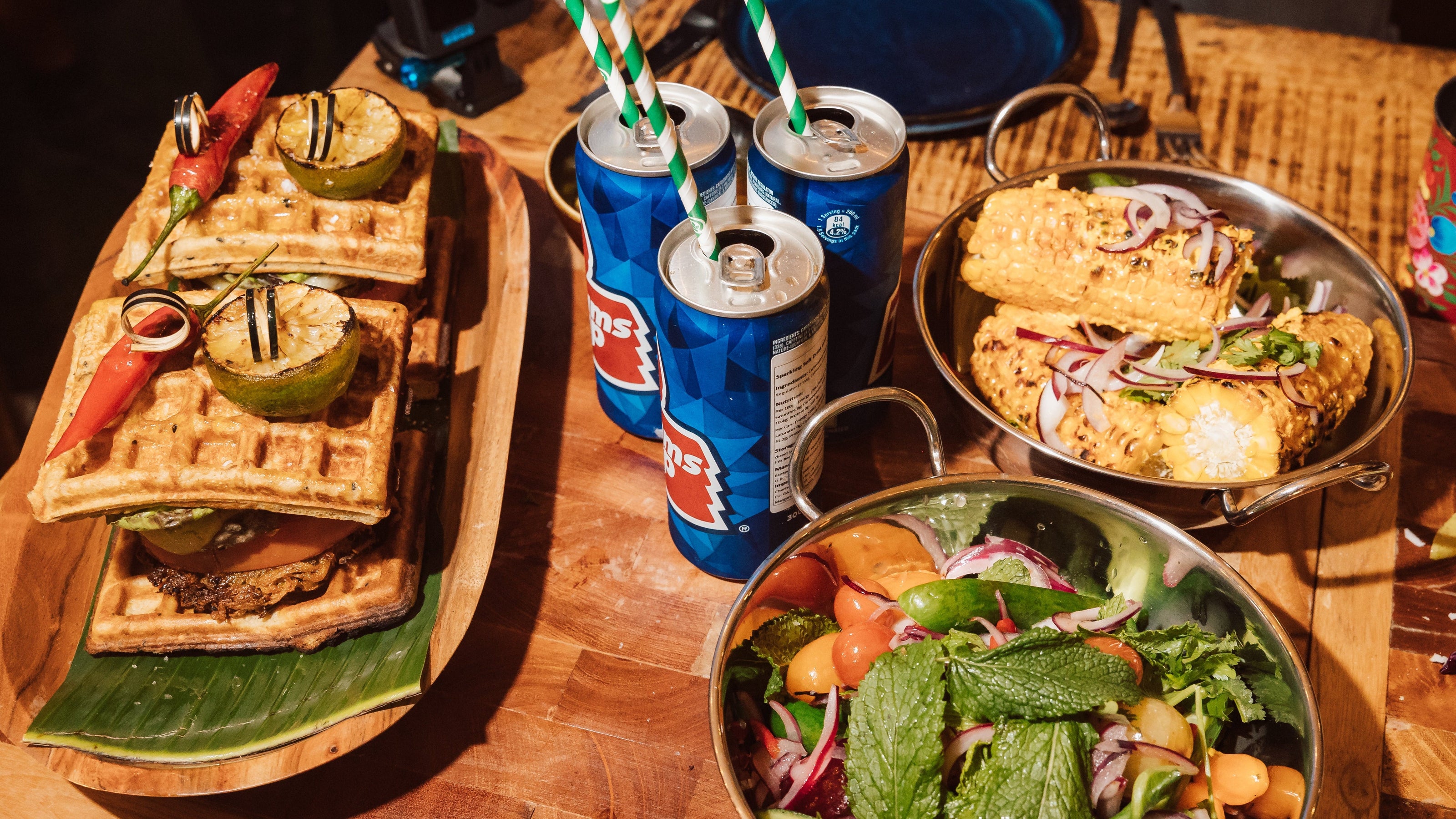 Diverse food items including waffles, tacos, and a salad on a wooden table with drinks.
