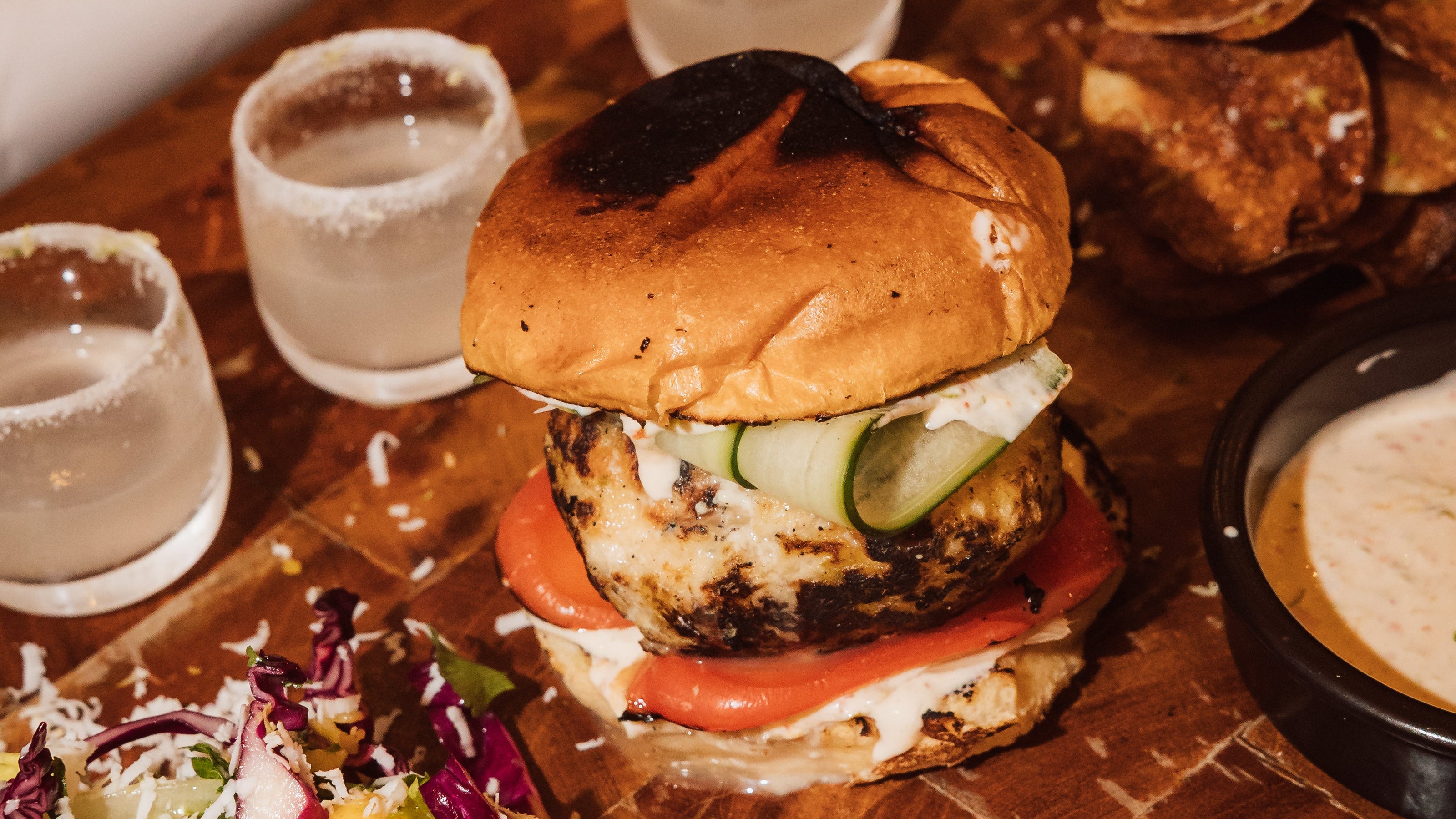 Hamburger with toppings on a wooden table with drinks and a can of Red Bull.