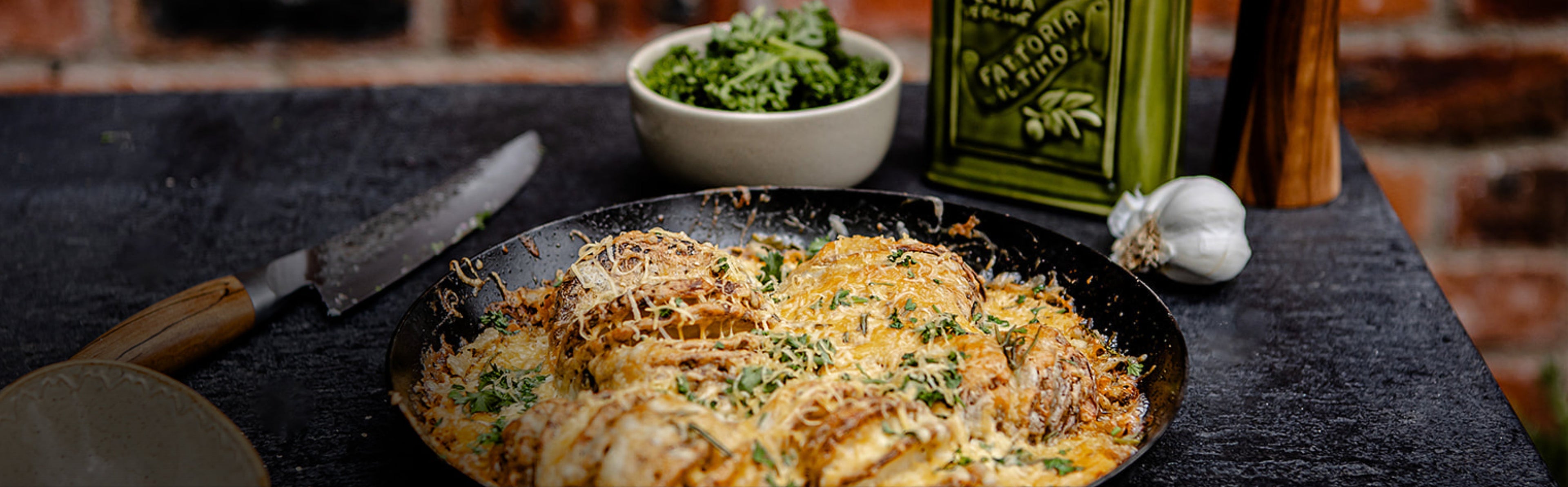 Dish of baked potatoes with cheese and herbs on a dark surface with a brick wall background
