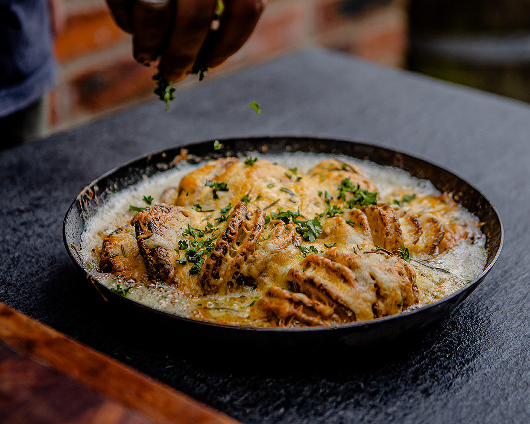 Fried food in a kadai oven dish with a person seasoning it, on a garden kitchen