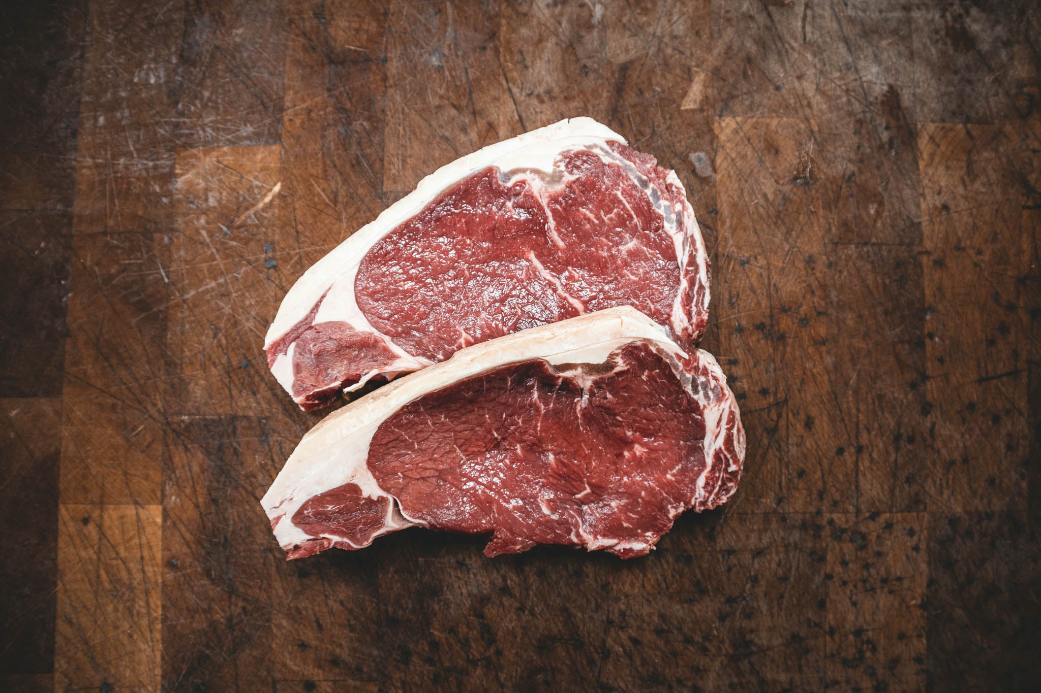 Two raw steak pieces on a wooden cutting board