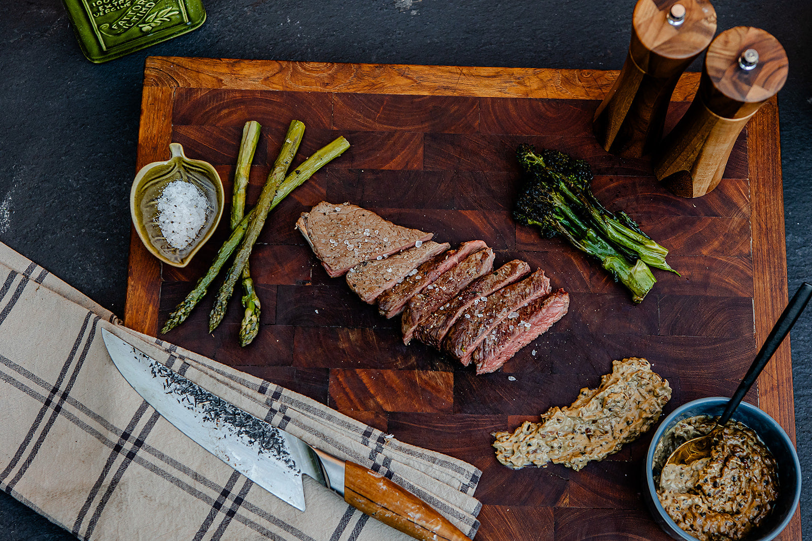 Sliced steak on a kadai butchers block with asparagus, bread, and condiments.
