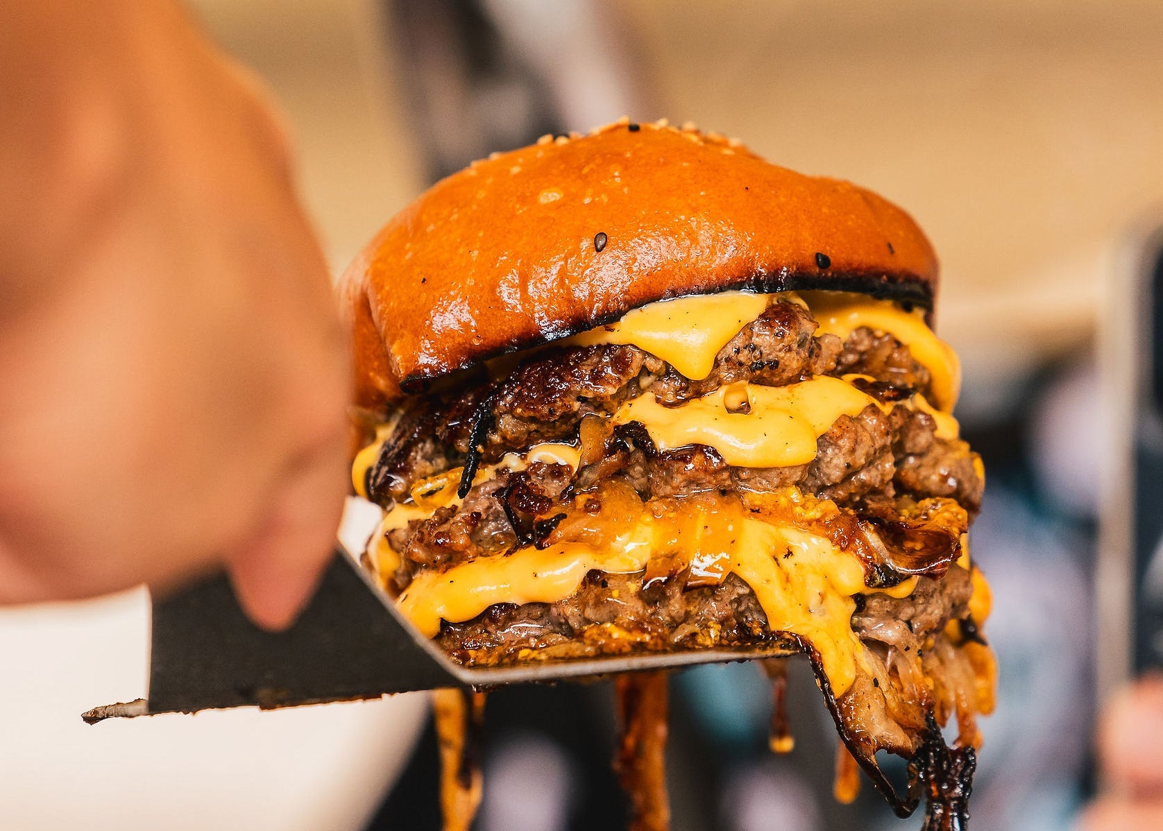 Hand holding a large, juicy burger with cheese and lettuce against a blurred background