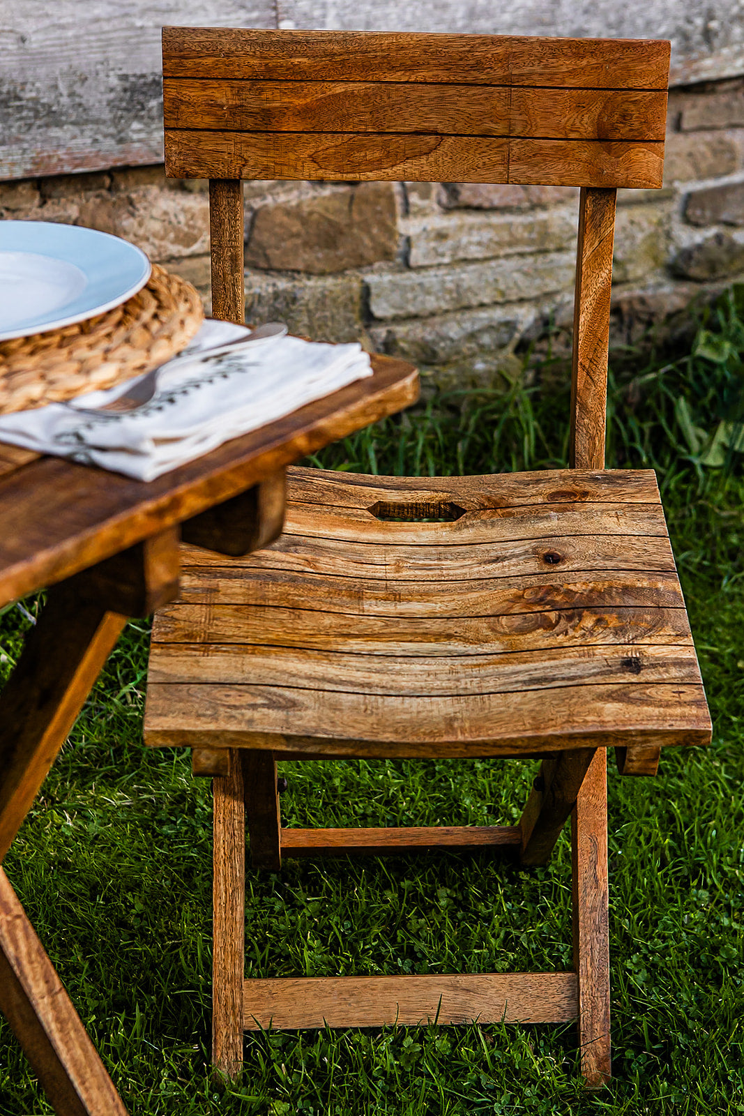 Handcrafted folding café chair made from natural wood, styled next to a rustic outdoor table setting with stone wall backdrop