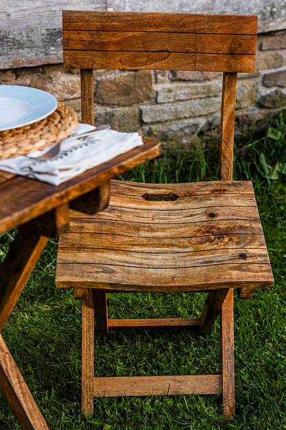 Handcrafted folding café chair made from natural wood, styled next to a rustic outdoor table setting with stone wall backdrop