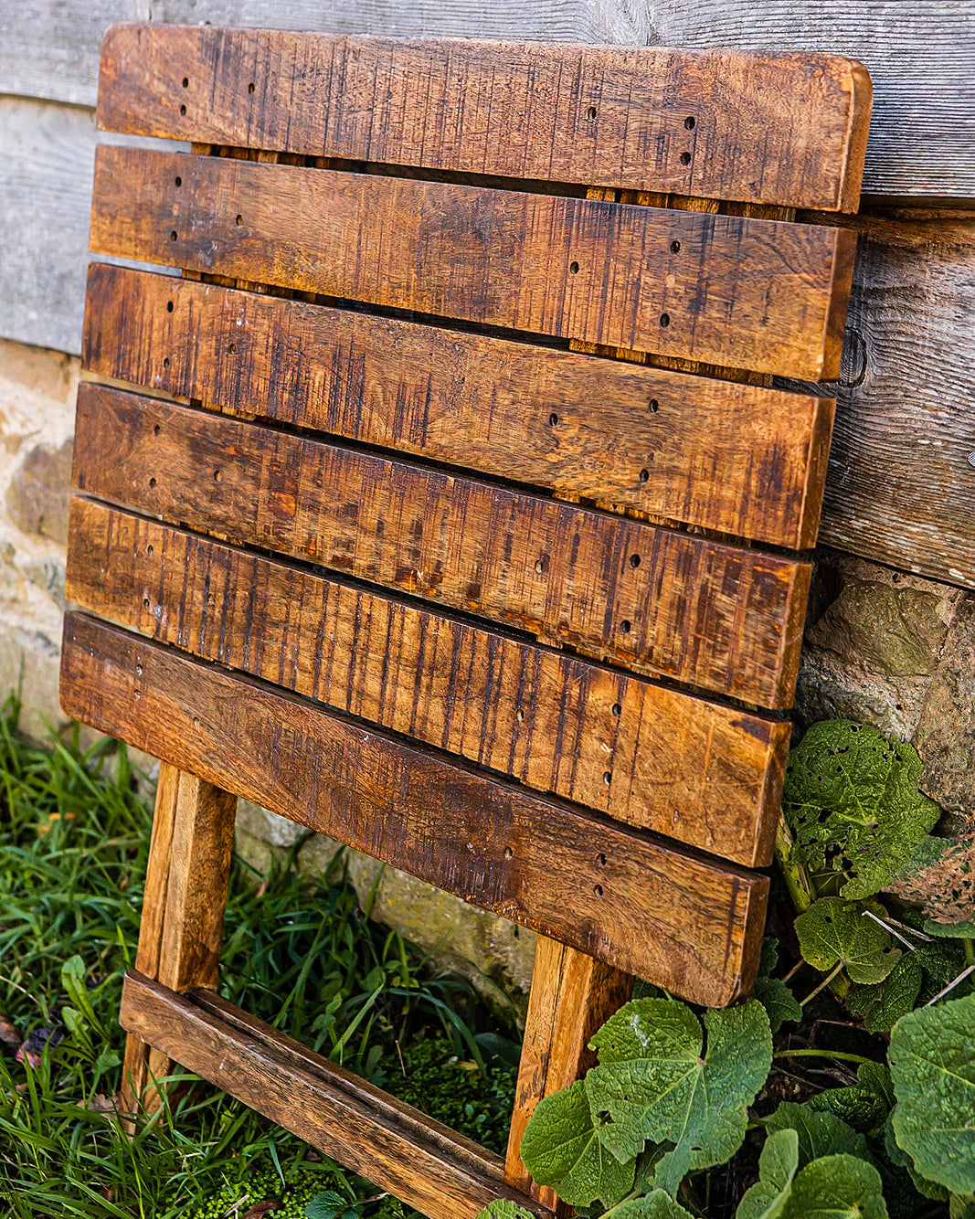 Rustic foldable wooden café table with slatted design leaning outdoors beside a timber and stone wall
