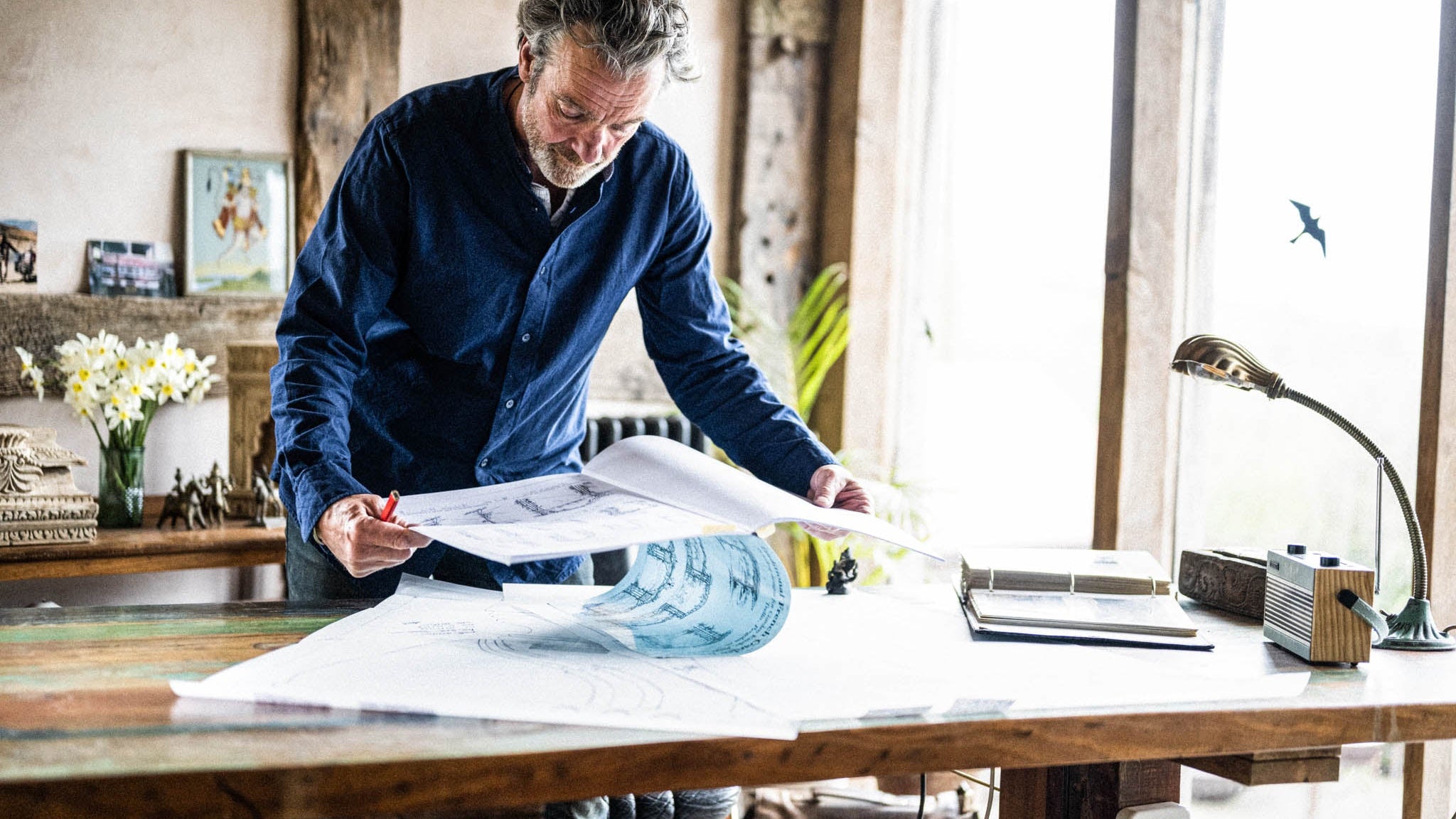 Christo Mckinnon founder of Kadai working on blueprints at a desk in a bright room with large windows.