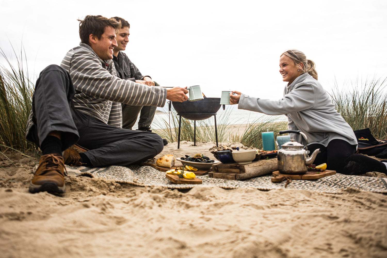 Friends enjoying food and drinks around a beach kadai travel fire bowl.