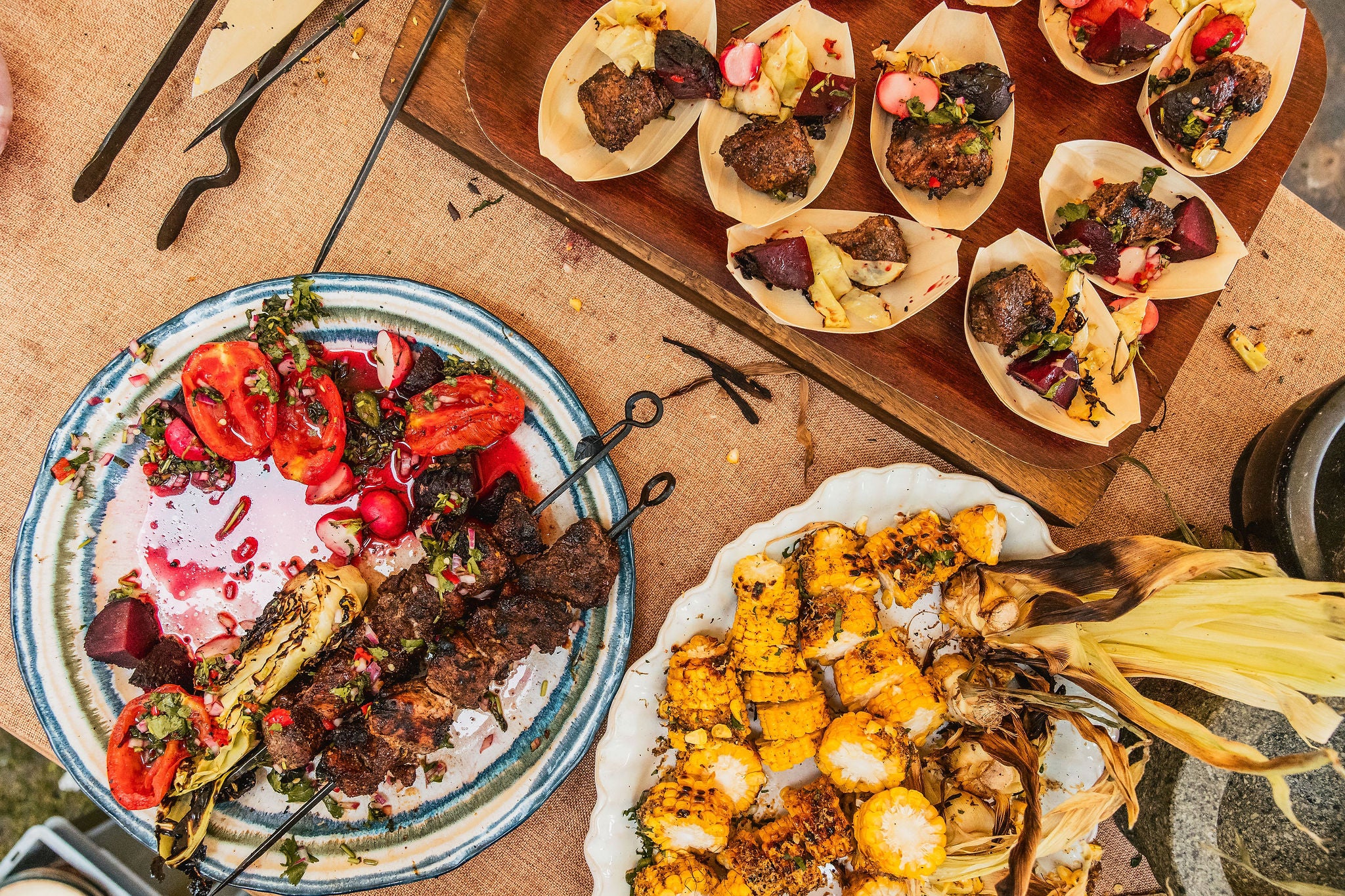 Plates of food with grilled vegetables and meat on a wooden board.