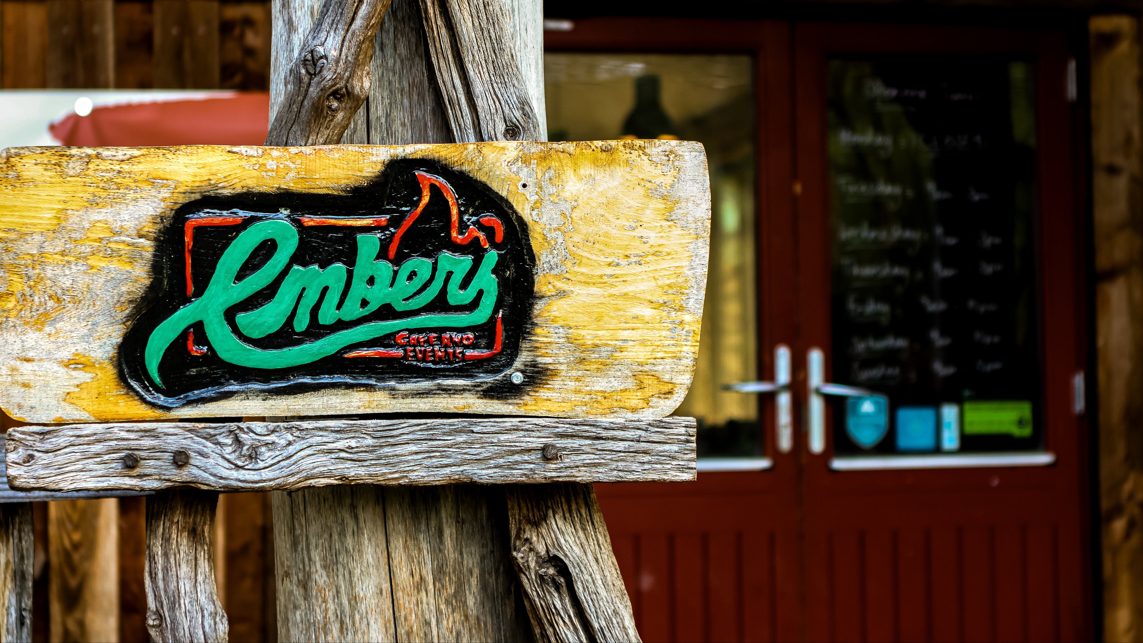 Wooden sign with 'Embers' logo in front of a rustic wooden building.