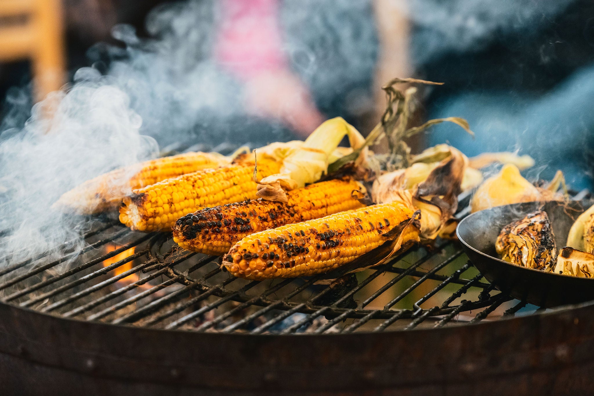 Grilled corn on a barbecue with smoke and a blurred background