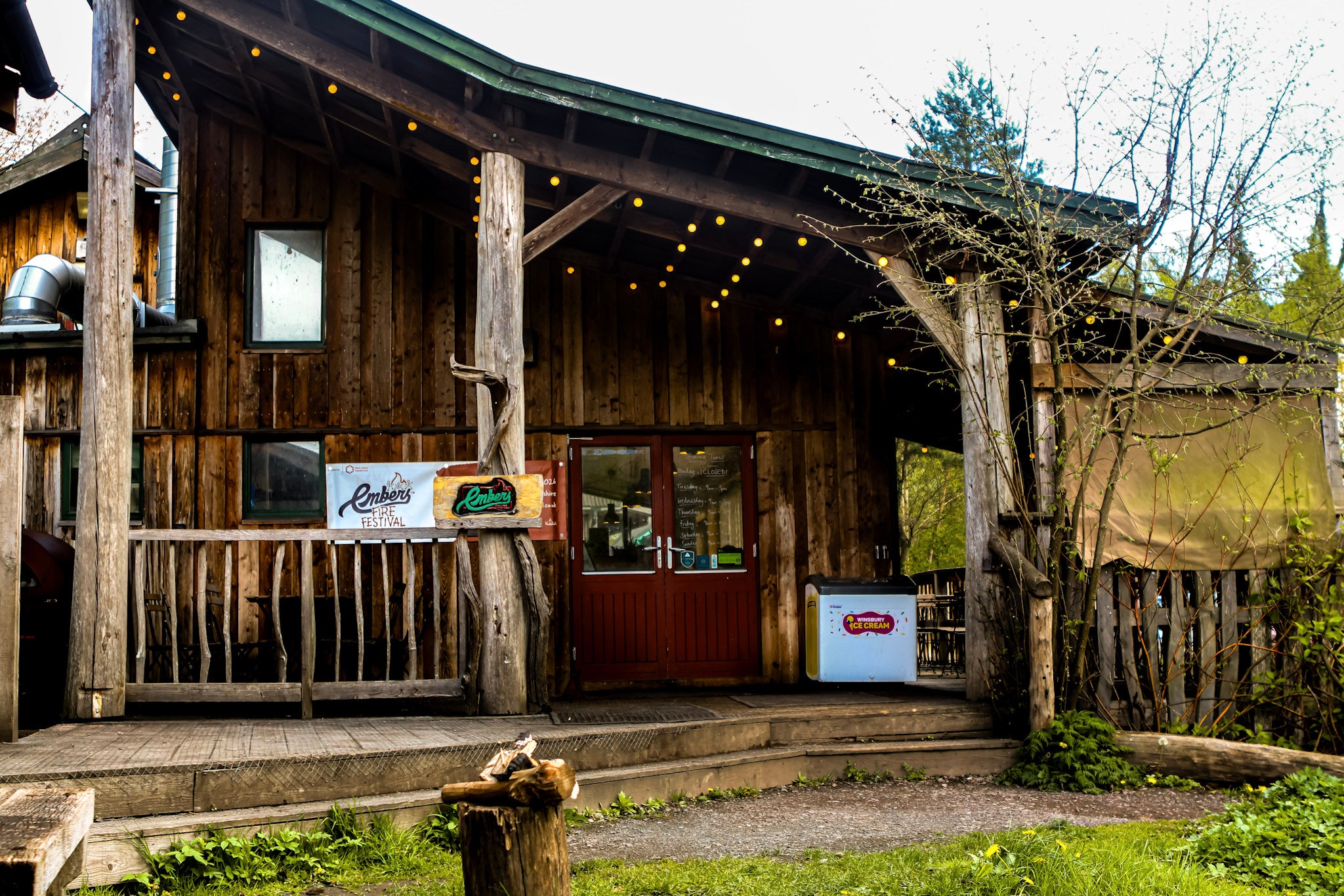 Wooden cabin with a porch and signs saying Embers on a grassy area