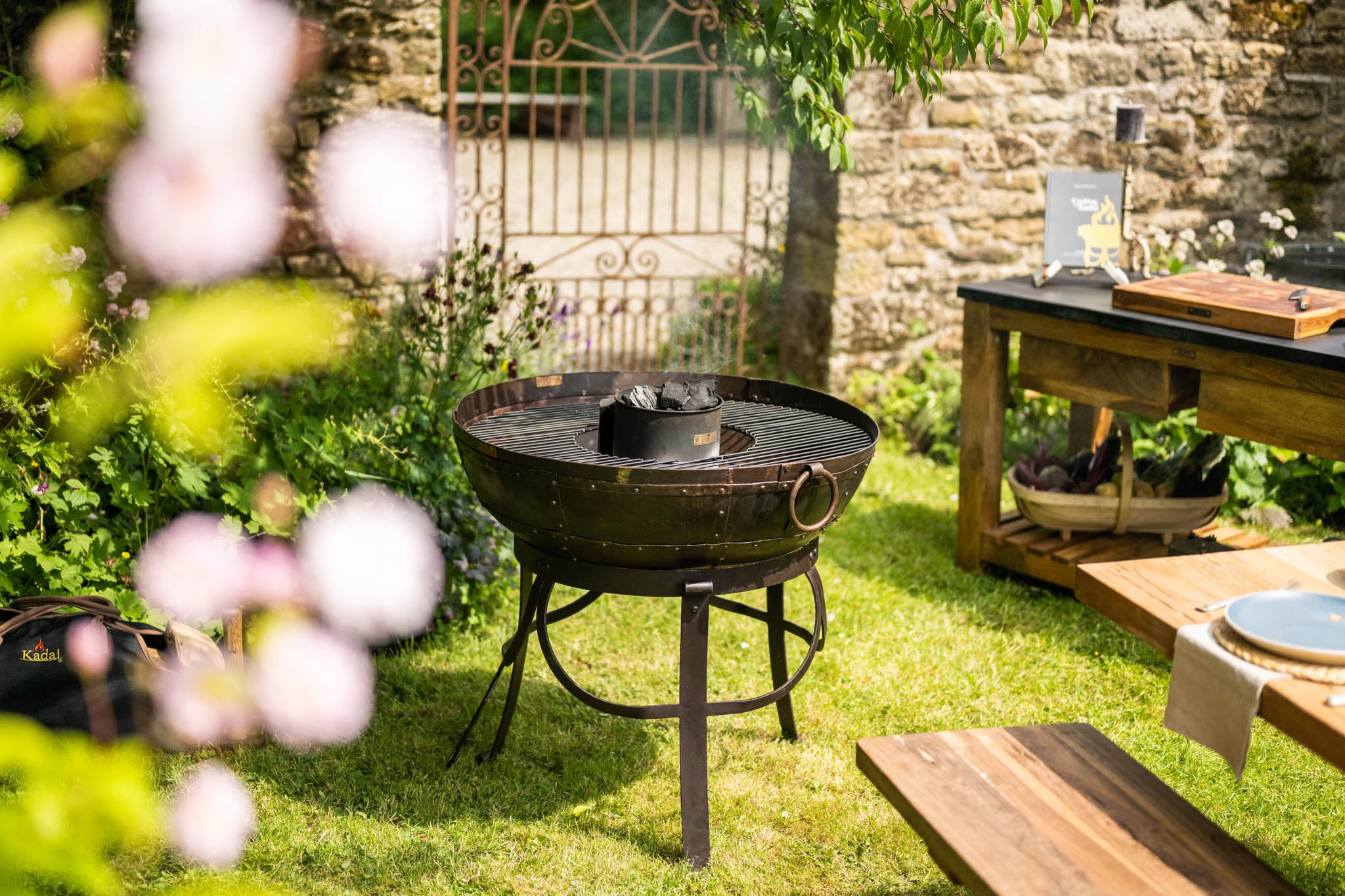 Outdoor garden setting with a Kadai BBQ fire pit and wooden garden furniture.