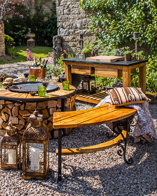 Curved wooden outdoor bench beside a rustic fire pit dining area in a garden patio