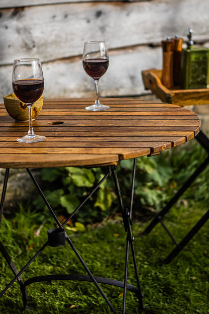 Two glasses of red wine on a wooden table outdoors in a garden.