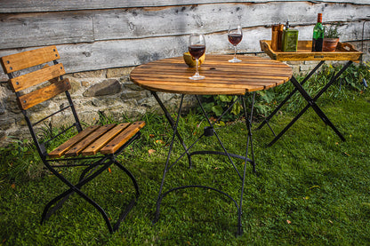 Garden table with chairs and wine glasses on a grassy area with a rustic wooden wall background.