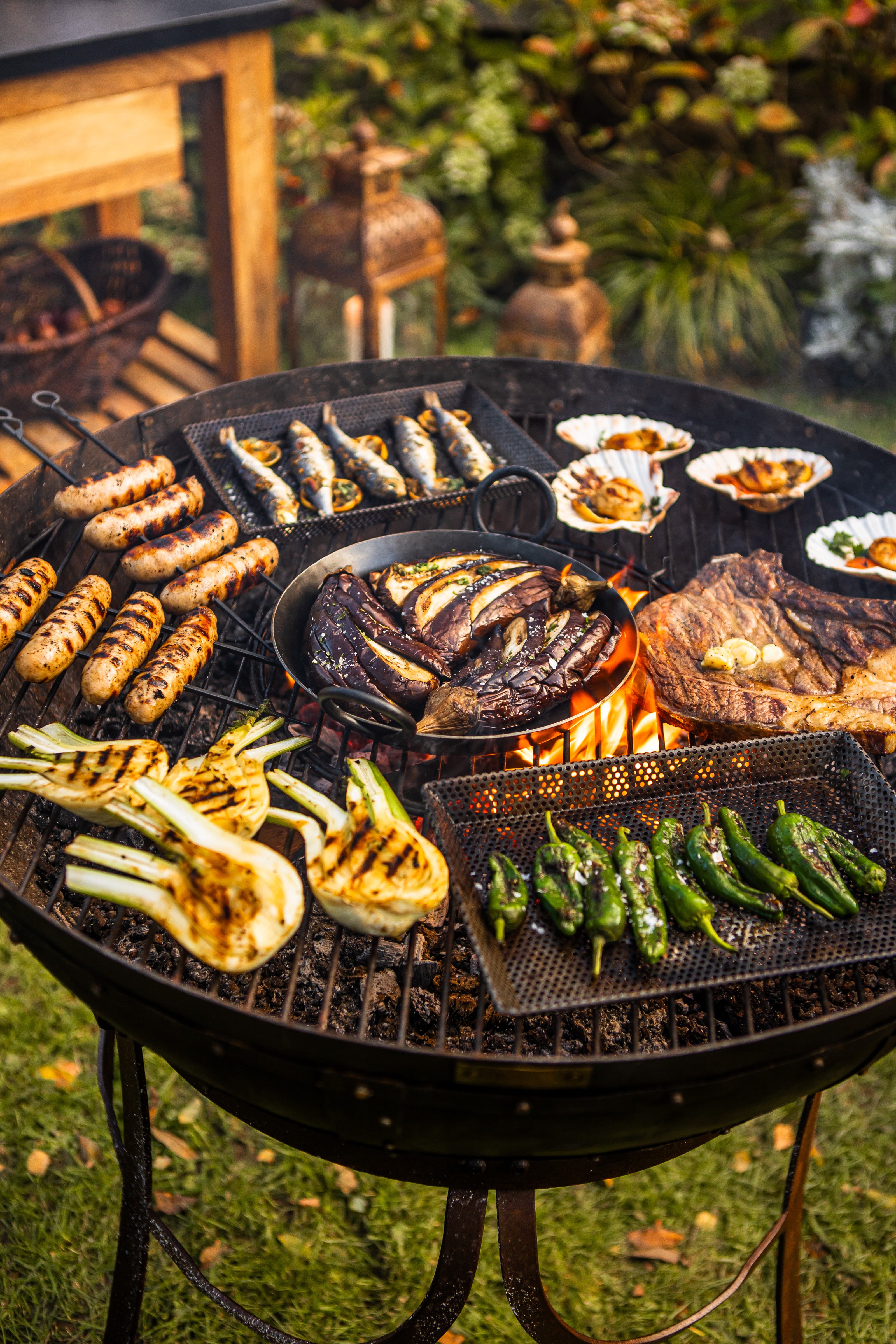 Outdoor grill with various meats, vegetables, and skewers on a grassy area.