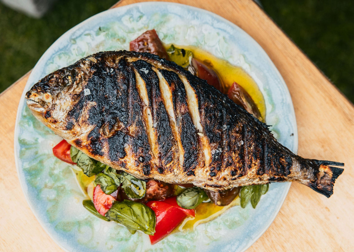 A Grilled Fish on a plate with fresh basil and tomatoes