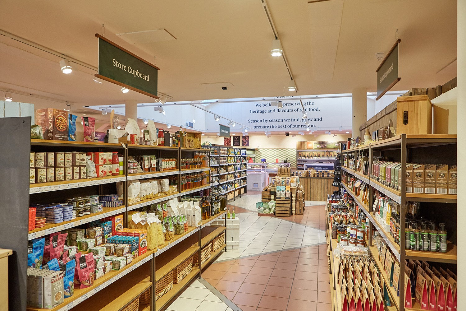 Supermarket interior with shelves stocked with products and a large screen on the wall.