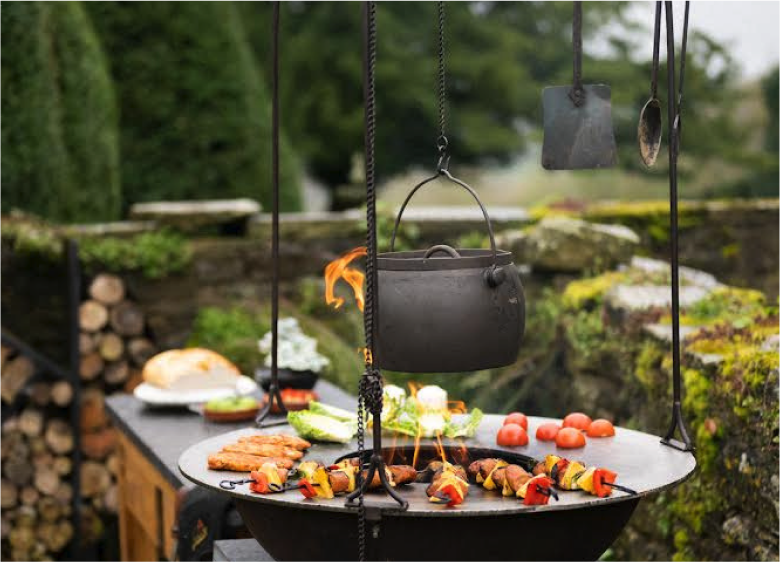 Kadai firepit with hanging kettle cooking skewers and vegetables outdoors