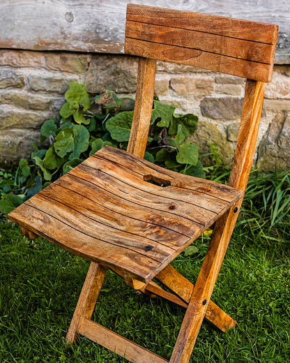 Handcrafted folding café chair made from natural wood, styled outdoors in a rustic garden setting