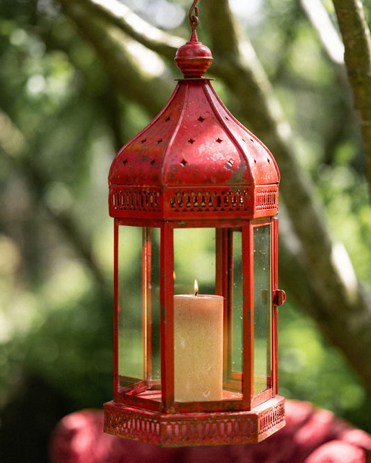 Red lantern with a candle inside, held by a hand against a blurred natural background