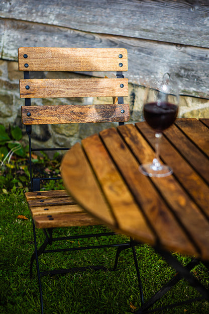 Wooden outdoor table with a garden folding chair and glass of red wine on a grassy area.