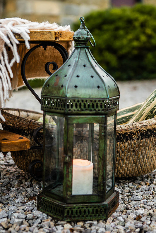 Decorative lantern with a candle on pebbles, surrounded by wicker baskets and greenery.