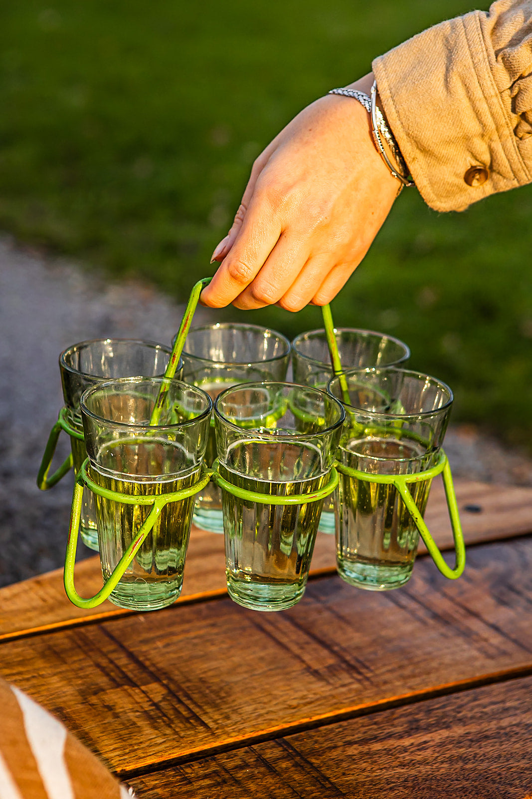 Set of chai glasses in green metal holder being carried by hand over wooden outdoor table