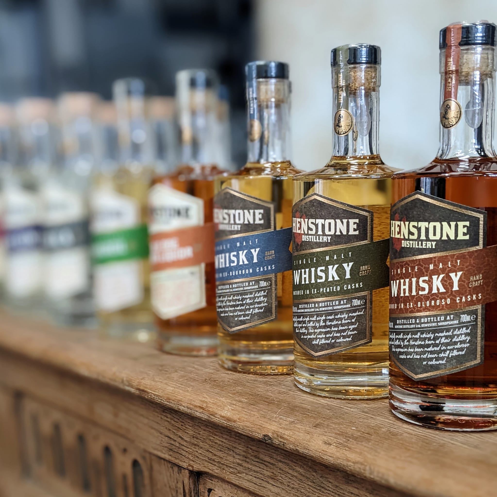 Row of Henstone Distillery whisky bottles on a wooden shelf.