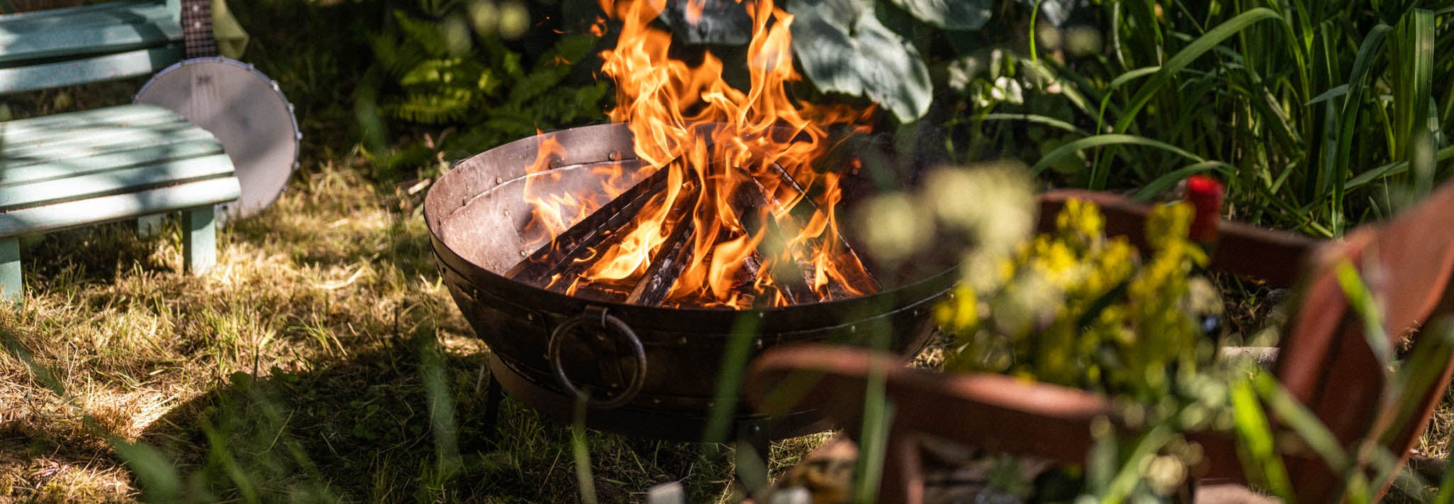 Fire pit with flames in a garden setting with chairs and plants