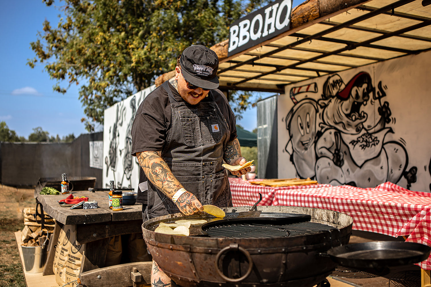 Person grilling on a Kadai at a Beef Stock BBQ event with a branded canopy in the background