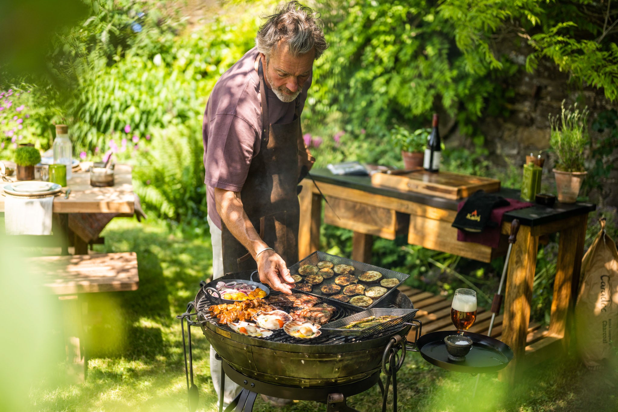 Man cooking outdoors on a Kadai barbecue with grilled food
