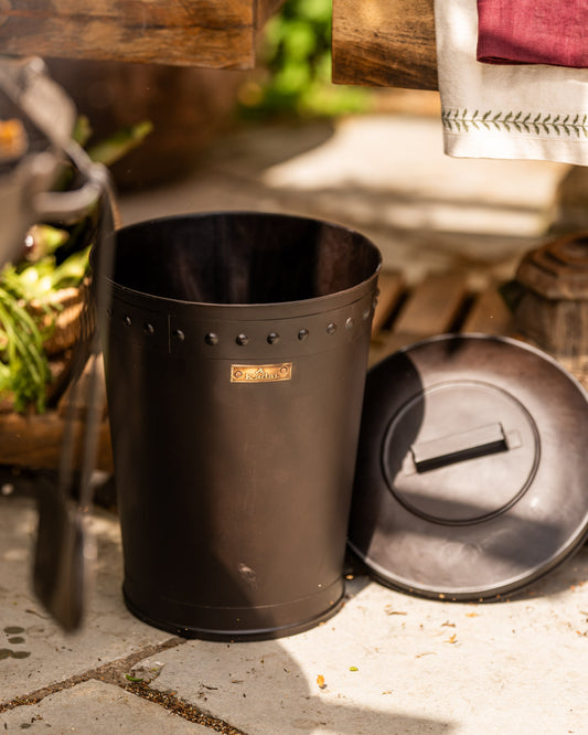Black BBQ bin with removable lid beside a Kadai firebowl barbecue in an outdoor cooking area