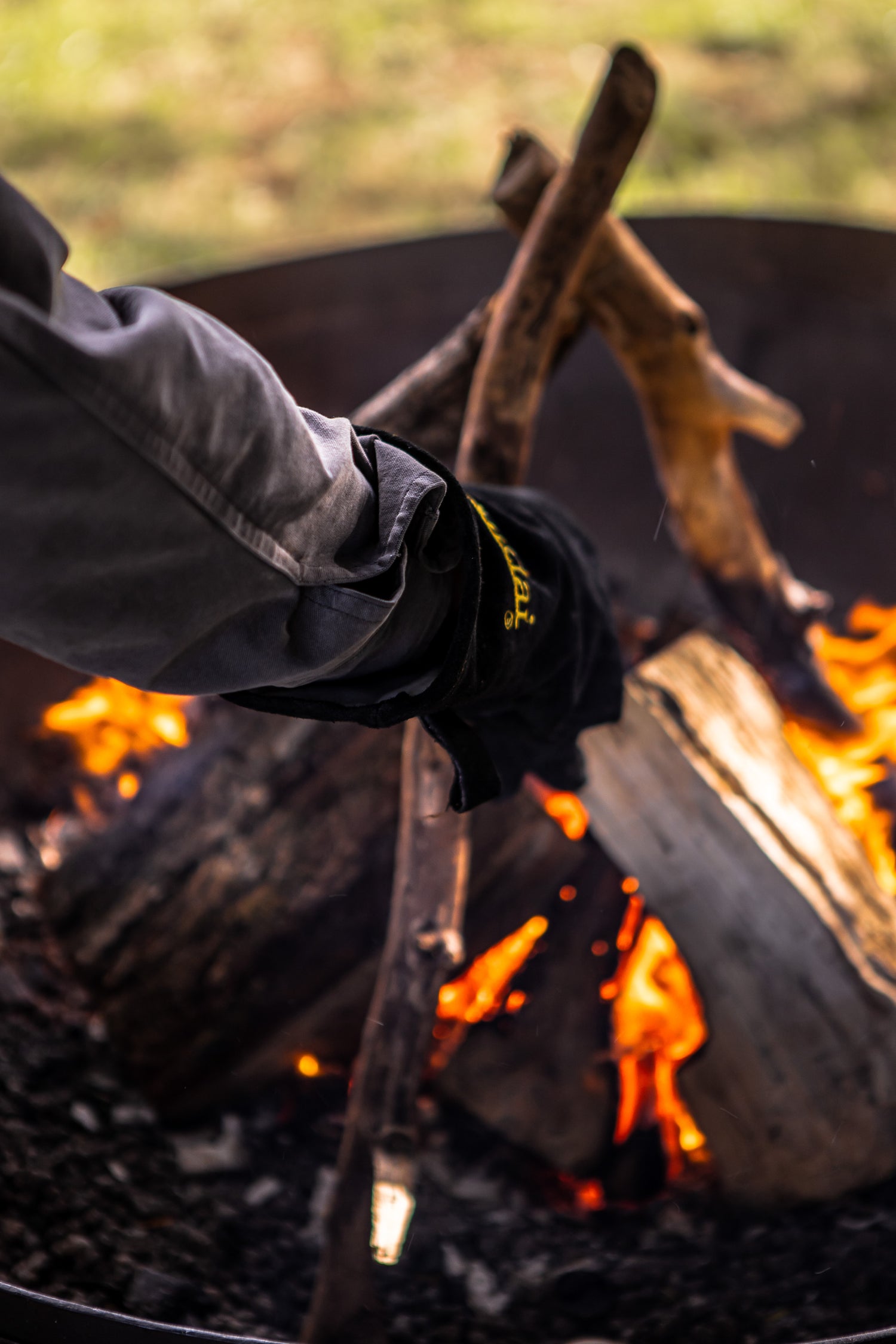 Person wearing a black glove holding a log over a kadai campfire