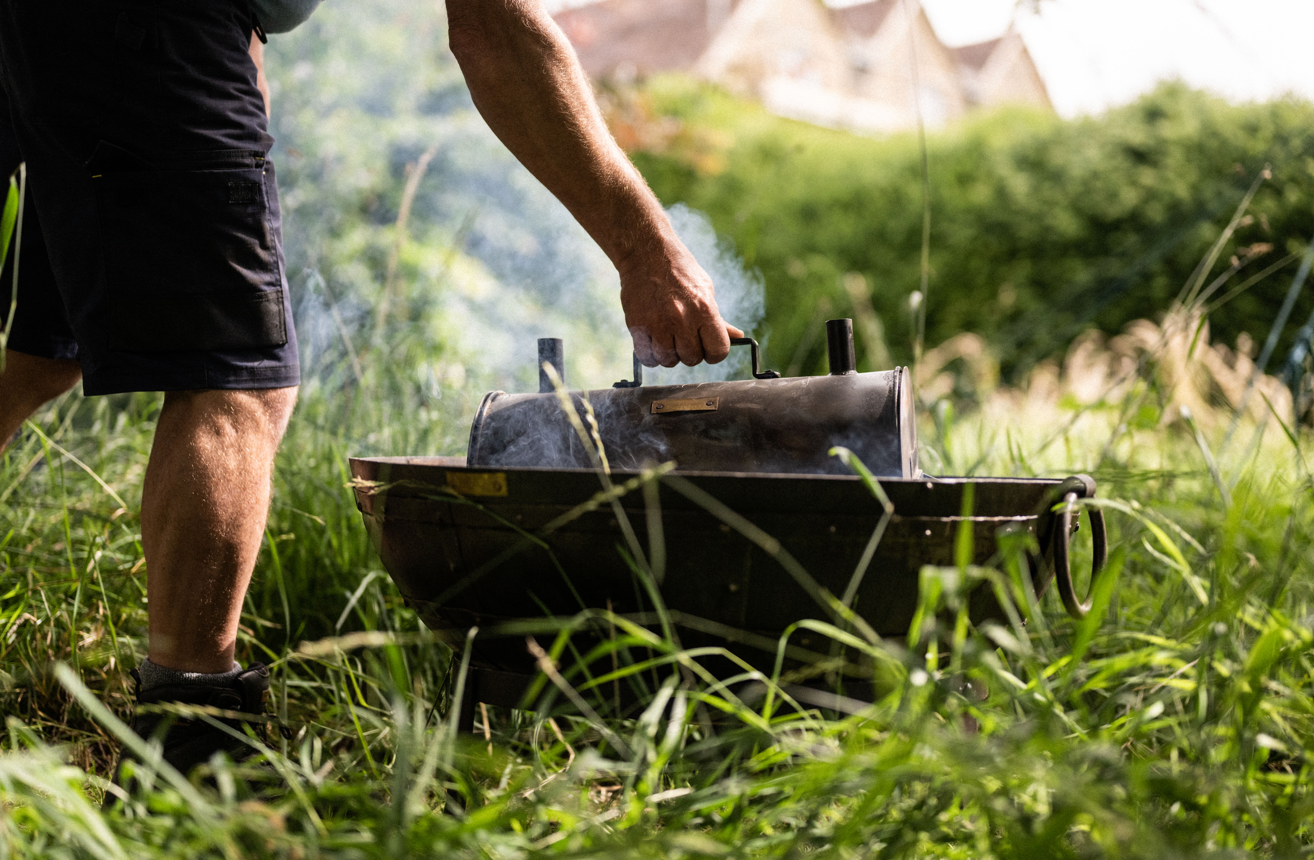 Kadai Firebowl with man placing a charcoal maker in the bowl with a house and garden in the background.