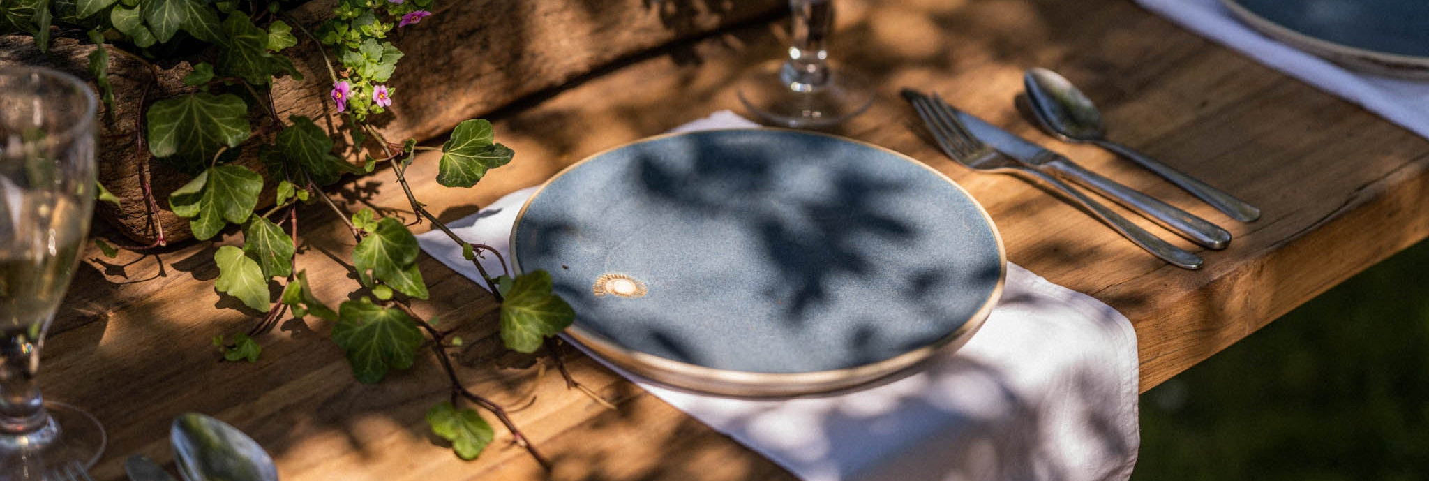 Dining table setting with blue plates, silverware, and floral decorations on a wooden surface.