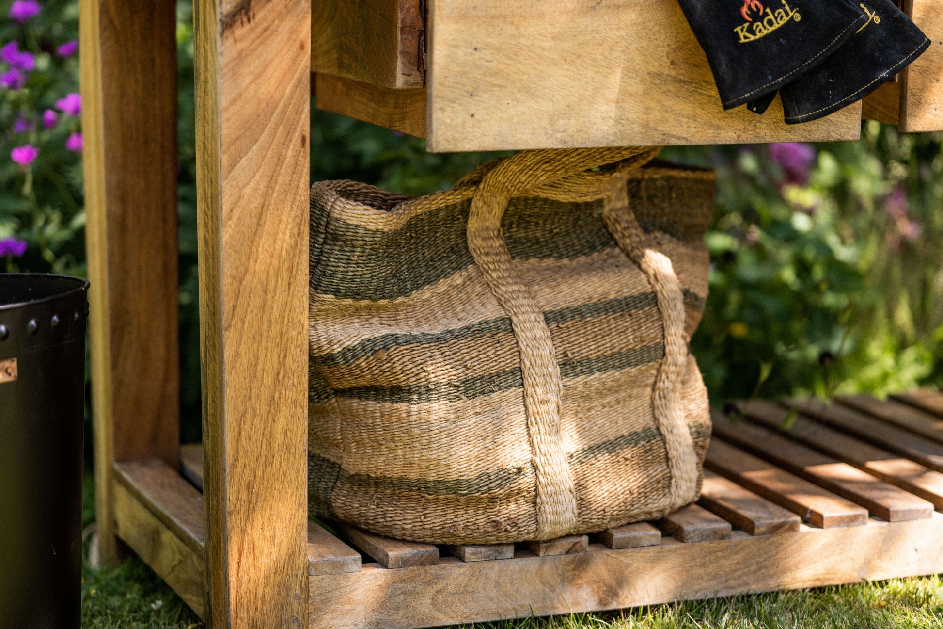Woven basket on a wooden shelf outdoors with blurred flowers in the background