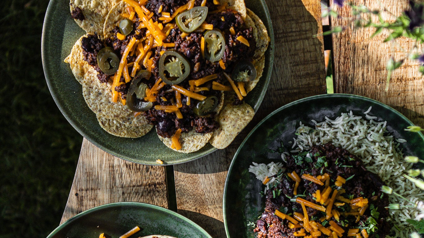 Three green plates with chilli con carne three ways on a wooden surface outdoors